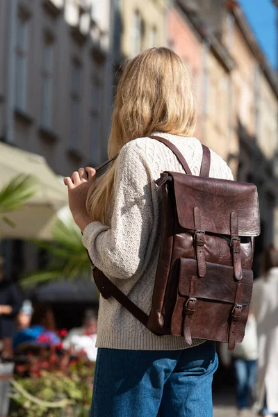 Woman with a brown leather backpack with antique and retro look. Outdoors photo.