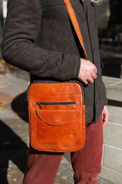 part photo of a man with orange leather bag . outdoors photo
