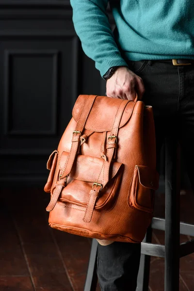 Orange leather oldfashioned backpack in a mans hands. indoors