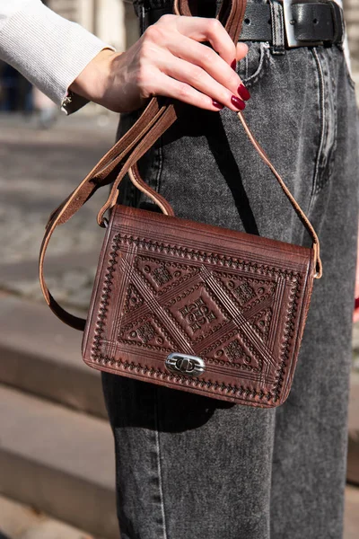 small brown womens leather bag with a carved pattern. street photo