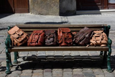 Tahta bir bankta farklı renkte deri sırt çantaları.