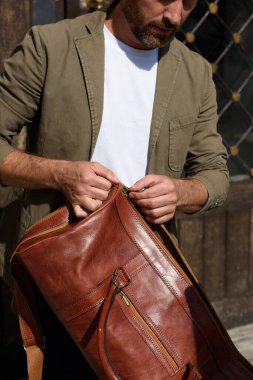 Çantası olan bir adam. siyah deri seyahat çantası, sokak fotoğrafı. Adam mavi spor ayakkabı, kot pantolon, beyaz tişört ve ceket giyiyor..