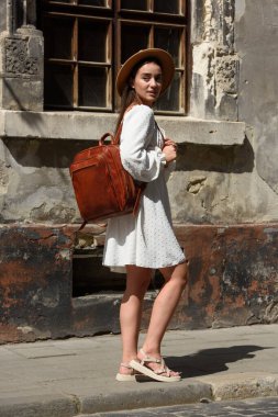 Esmer, uzun saçlı, beyaz elbiseli, bej şapkalı, lüks deri çantalı. Eski şehir sokağı. Tatil, turizm ve seyahat