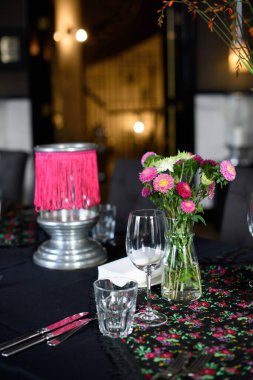 Bardaklar, çiçekler, çatal, bıçak restoranda servis ediliyor..