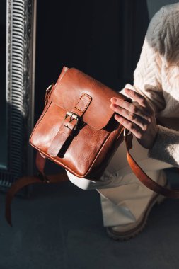 Sarı kıvırcık saçlı, kahverengi çantalı, gri arka planda poz veren güzel bir kadının stüdyo portresi. Şık bir şapka, süveter ve klasik pantolon giyiyor.