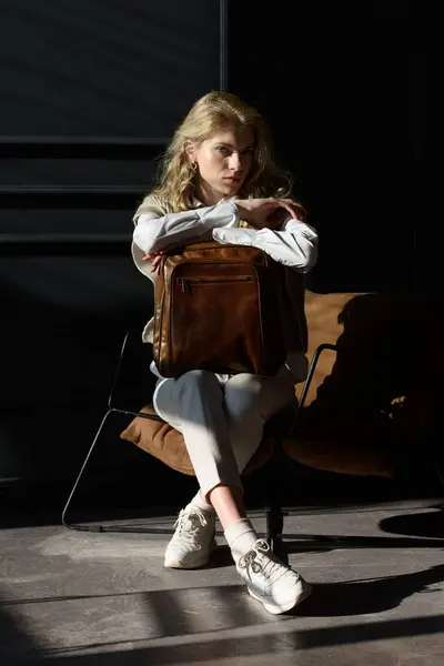 A woman holds leather backpack. Model wearing stylish knitted vest, white shirt and classic trousers.
