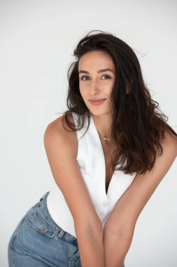 Yeni bir yaz havasında poz veren mutlu güzel kız. Kot pantolon ve beyaz yelek giyiyor..