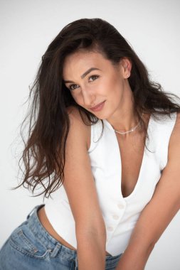 Yeni bir yaz havasında poz veren mutlu güzel kız. Kot pantolon ve beyaz yelek giyiyor..