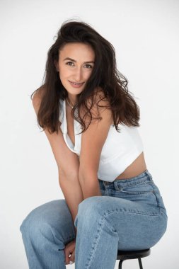 Yeni bir yaz havasında poz veren mutlu güzel kız. Kot pantolon ve beyaz yelek giyiyor..