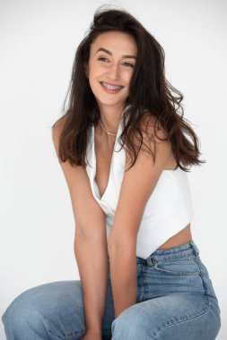 Yeni bir yaz havasında poz veren mutlu güzel kız. Kot pantolon ve beyaz yelek giyiyor..