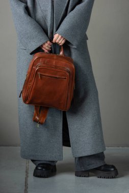 Deri sırt çantalı, gri ceketli ve siyah çizmeli bir kadın..