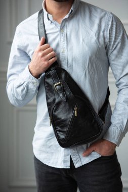 Omzunda siyah bir çanta taşıyan gömlekli bir adam.