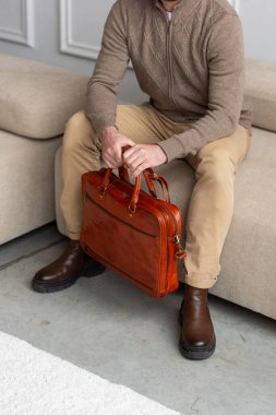 Bir adam koltukta rahat bir şekilde oturuyor ve yanında bir evrak çantası var. Etrafında rahat ve rahat bir ortam yaratıyor.