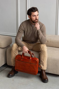Bir adam koltukta rahat bir şekilde oturuyor ve yanında bir evrak çantası var. Etrafında rahat ve rahat bir ortam yaratıyor.