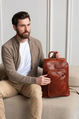 Zarif bir adam sarı kahverengi bir sırt çantasıyla çağdaş bir odada oturur, kentsel tarzı ve profesyonelliği somutlaştırır..