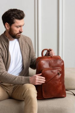 Zarif bir adam sarı kahverengi bir sırt çantasıyla çağdaş bir odada oturur, kentsel tarzı ve profesyonelliği somutlaştırır..
