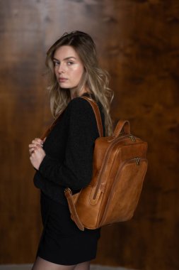 Sıcak kazaklı, siyah kısa etekli ve naylon taytlı bir kız açık kahverengi bir sırt çantasıyla poz veriyor.