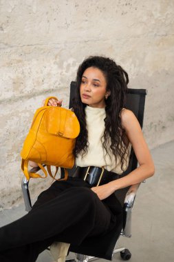 Moda modasına uygun bir model, canlı sarı bir sırt çantası ile modern bir kıyafet sergiliyor.