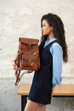 Moda modasına uygun bir model, kahverengi bir sırt çantası ile modern bir kıyafet sergiliyor.
