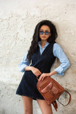 Moda modasına uygun bir model, kahverengi bir sırt çantası ile modern bir kıyafet sergiliyor.