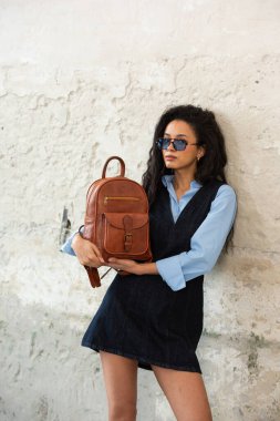 Moda modasına uygun bir model, kahverengi bir sırt çantası ile modern bir kıyafet sergiliyor.