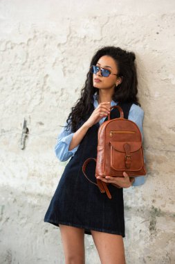 Moda modasına uygun bir model, kahverengi bir sırt çantası ile modern bir kıyafet sergiliyor.