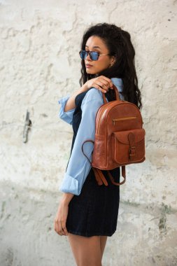 Moda modasına uygun bir model, kahverengi bir sırt çantası ile modern bir kıyafet sergiliyor.