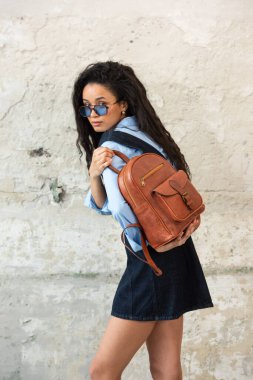 Moda modasına uygun bir model, kahverengi bir sırt çantası ile modern bir kıyafet sergiliyor.