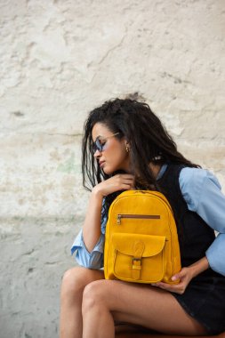 Modaya uygun bir model, sarı bir sırt çantası ve aksesuarla modern bir kıyafet sergiliyor.