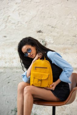 Modaya uygun bir model, sarı bir sırt çantası ve aksesuarla modern bir kıyafet sergiliyor.