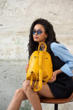 Modaya uygun bir model, sarı bir sırt çantası ve aksesuarla modern bir kıyafet sergiliyor.