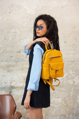 Modaya uygun bir model, sarı bir sırt çantası ve aksesuarla modern bir kıyafet sergiliyor.