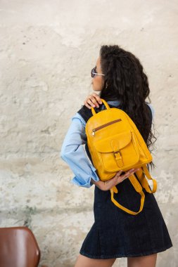 Modaya uygun bir model, sarı bir sırt çantası ve aksesuarla modern bir kıyafet sergiliyor.