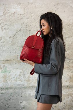 Gri bir ceket giyiyorlar ve gri bir etek giyiyorlar, soluk beyaz bir duvara karşı..