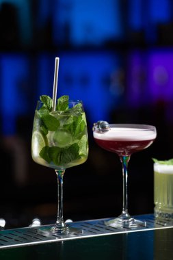 Bar masasında çeşitli renkli alkollü kokteyller. Süslü bir arka planda farklı şekillerde gözlük