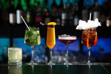 Bar masasında çeşitli renkli alkollü kokteyller. Süslü bir arka planda farklı şekillerde gözlük