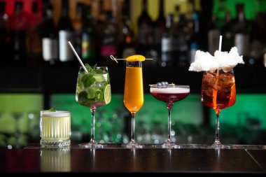 Bar masasında çeşitli renkli alkollü kokteyller. Süslü bir arka planda farklı şekillerde gözlük