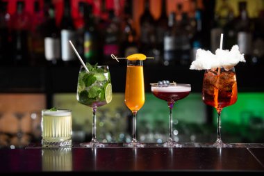 Bar masasında çeşitli renkli alkollü kokteyller. Süslü bir arka planda farklı şekillerde gözlük