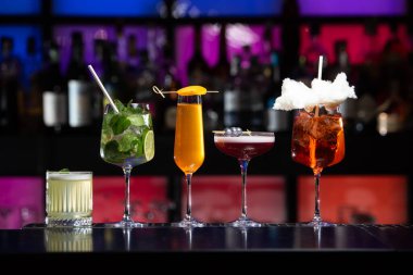 Bar masasında çeşitli renkli alkollü kokteyller. Süslü bir arka planda farklı şekillerde gözlük