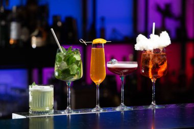 Bar masasında çeşitli renkli alkollü kokteyller. Süslü bir arka planda farklı şekillerde gözlük