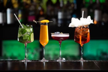 Bar masasında çeşitli renkli alkollü kokteyller. Süslü bir arka planda farklı şekillerde gözlük
