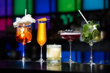 Bar masasında çeşitli renkli alkollü kokteyller. Süslü bir arka planda farklı şekillerde gözlük