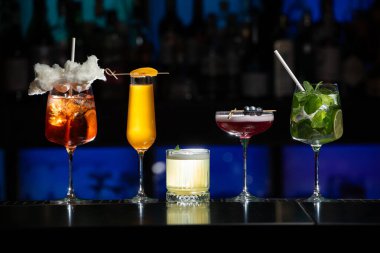 Bar masasında çeşitli renkli alkollü kokteyller. Süslü bir arka planda farklı şekillerde gözlük