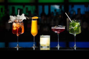 Bar masasında çeşitli renkli alkollü kokteyller. Süslü bir arka planda farklı şekillerde gözlük