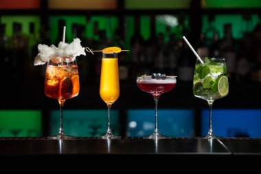 Bar masasında çeşitli renkli alkollü kokteyller. Süslü bir arka planda farklı şekillerde gözlük