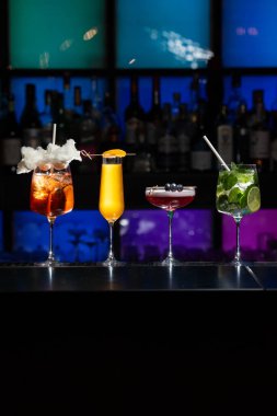Bar masasında çeşitli renkli alkollü kokteyller. Süslü bir arka planda farklı şekillerde gözlük