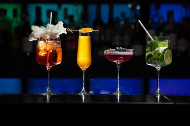 Bar masasında çeşitli renkli alkollü kokteyller. Süslü bir arka planda farklı şekillerde gözlük