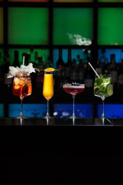 Bar masasında çeşitli renkli alkollü kokteyller. Süslü bir arka planda farklı şekillerde gözlük
