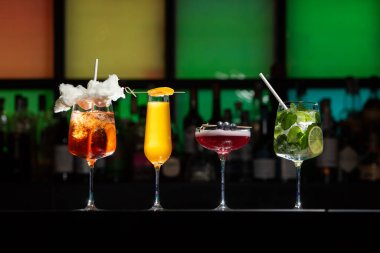 Bar masasında çeşitli renkli alkollü kokteyller. Süslü bir arka planda farklı şekillerde gözlük