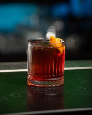 Koyu kırmızı alkollü buzlu kokteyl ve portakal kabuklu garnitür buzlu bir bardakta sunuluyor.